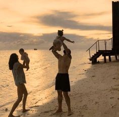 a man holding a baby up in the air while standing next to two women on a beach