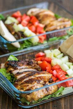 two glass dishes filled with chicken, lettuce and tomatoes on a wooden table