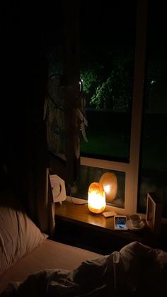 a bed in a dark room next to a window with a lit candle on it