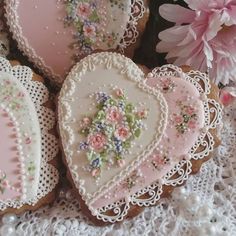 four decorated heart shaped cookies sitting on top of a lace doily next to pink flowers