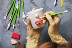 a person in gloves holding a cup with some candy on it and other tools around them