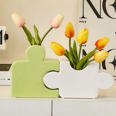 yellow and pink tulips are in a white vase on a shelf next to a clock