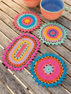 three crocheted coasters sitting on top of a wooden table next to two cups