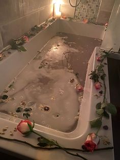 a bathtub filled with water and flowers next to a candle on the side of it