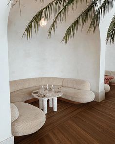 a corner table with two wine glasses on it in front of a white wall and wooden floor