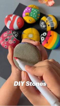 a person holding a rock in front of some colorful rocks on a table with the words diy stones above it