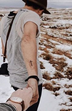 a man with a cross tattoo on his arm walking in the snow