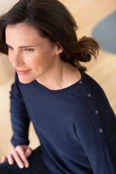 a woman sitting on top of a wooden floor wearing a blue shirt and black pants