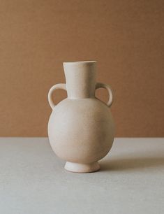 a white vase sitting on top of a table next to a brown wall in the background