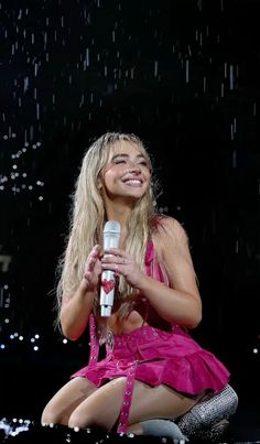 a woman sitting on the ground holding a microphone in front of rain falling down behind her