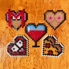 four pieces of bead art on a wooden surface with hearts and other items in them