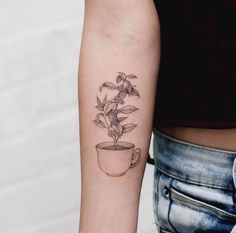 a woman with a tattoo on her arm holding a coffee cup filled with flowers and leaves