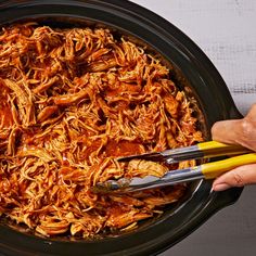 someone is using tongs to cut up noodles in the crock pot with meat