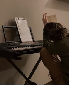 a woman sitting at a keyboard with her hand on top of the keyboard and holding an open sheet of paper