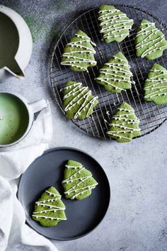 green cookies with white icing on a cooling rack next to a cup of tea