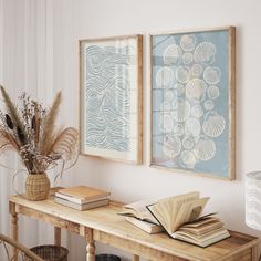 there are two framed pictures on the wall next to a table with books and plants