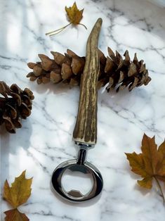 a bottle opener sitting on top of a marble counter next to pine cones and leaves