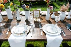 the table is set with plates, silverware and flowers in vases on it