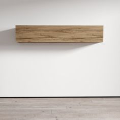 a wooden shelf mounted to the side of a white wall in an empty room with hard wood flooring