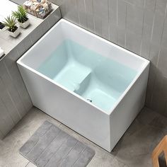 a bath tub sitting on top of a tiled floor next to a wooden chair and potted plant