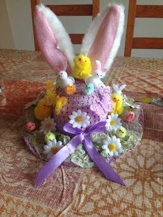 an easter cake decorated with bunny ears and flowers on a tablecloth covered dining room table