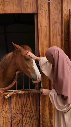 a woman is petting a horse in a stable while wearing a brown robe and headdress