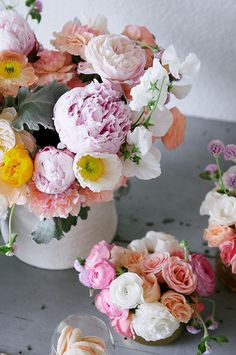 several different types of flowers in a white vase on a gray table with other flowers