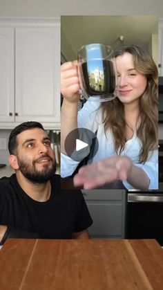 a man and woman sitting at a kitchen table holding up wine glasses in front of them