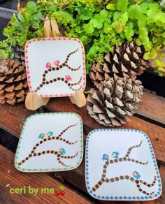 three decorative plates sitting on top of a wooden table next to pine cones and plants