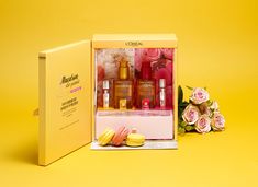 an open box containing several different types of beauty products and flowers on a yellow background