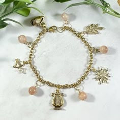 a gold bracelet with charms on it and flowers in the background, sitting on a marble surface