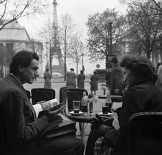 black and white photograph of two people sitting at an outdoor table in front of the eiffel tower