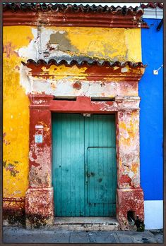 an old building with a green door in front of blue and yellow walls on the street