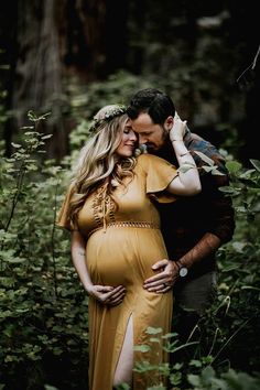 a pregnant woman in a yellow dress standing next to a man with his arm around her belly