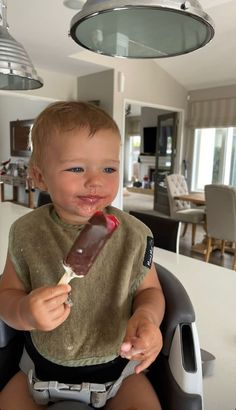 a baby sitting in a highchair eating an ice cream cone with chocolate on it