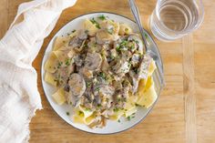 a white plate topped with pasta covered in mushroom sauce and parsley next to a glass of water