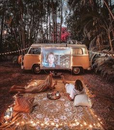 two people sitting on a blanket in front of a vw bus with a screen