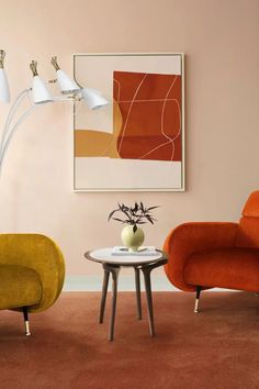 two orange chairs and a white table in a room with an art work on the wall