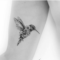 a small hummingbird with flowers on its back leg tattoo by the talented artist jane