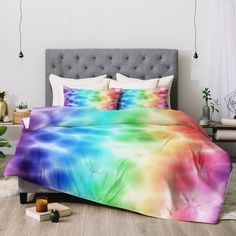 a bed with a rainbow colored comforter and pillows on top of it in a room