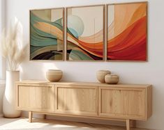 three paintings on the wall above a wooden cabinet