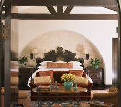 a large bed sitting under a wooden arch in a bedroom next to a table with flowers on it