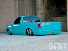 a blue pick up truck is parked in front of a concrete wall and brick building