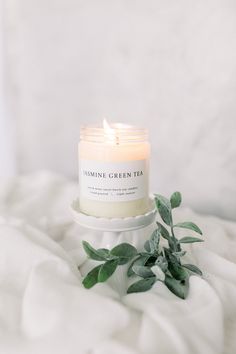 a white candle sitting on top of a bed next to a green leafy plant