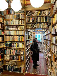 a woman standing in the middle of a library filled with books on shelves and lamps hanging from the ceiling