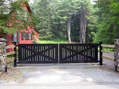 a black gate is in front of a red house and some trees on the other side