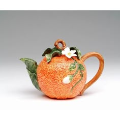 an orange shaped teapot with flowers on it