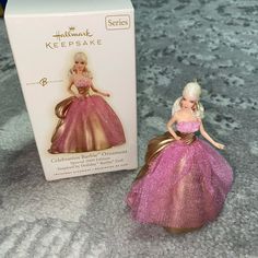 a pink and gold barbie doll next to a box