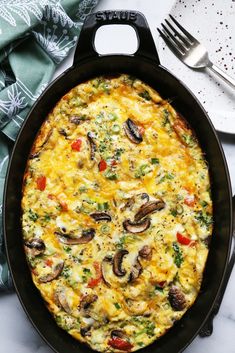 an omelet with mushrooms and vegetables in a black pan on a white table