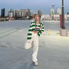 a woman standing in an empty parking lot wearing white pants and a green striped sweater